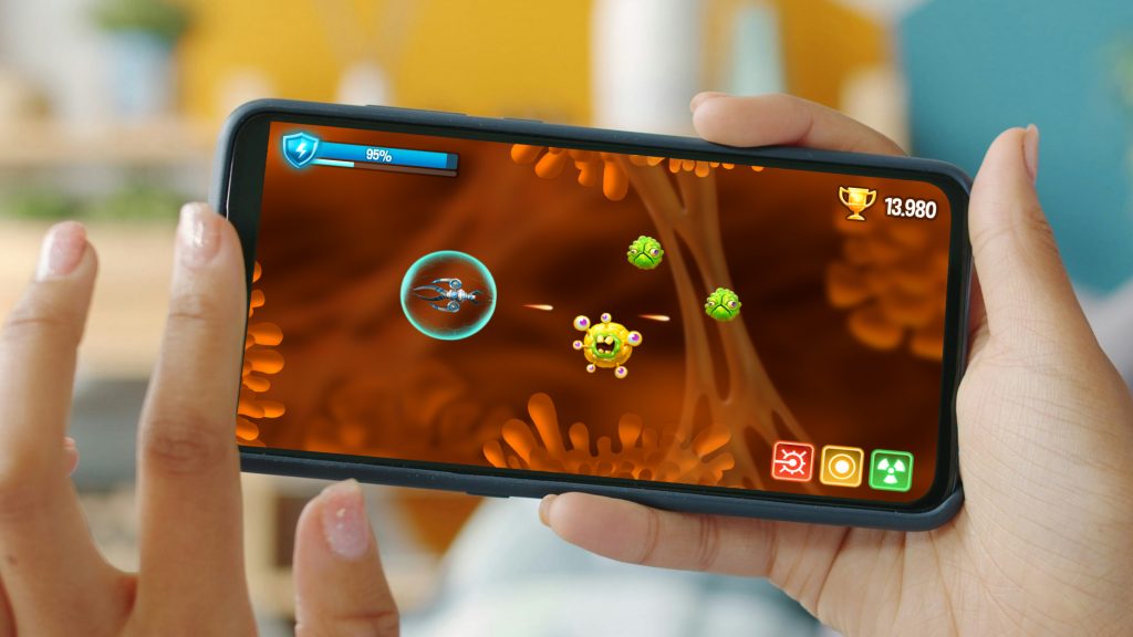 Screenshot of the I Manage Cancer shooter game on a smartphone in landscape format, depicting a submarine shooting at cancer cells in a stomach level.