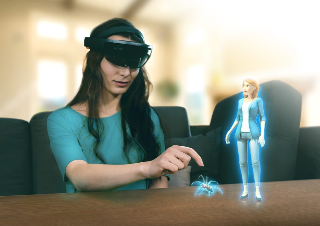 Photo of a person using the app with HoloLens device, as well as a virtual therapist character next to them on the table, together with the virtual spider.